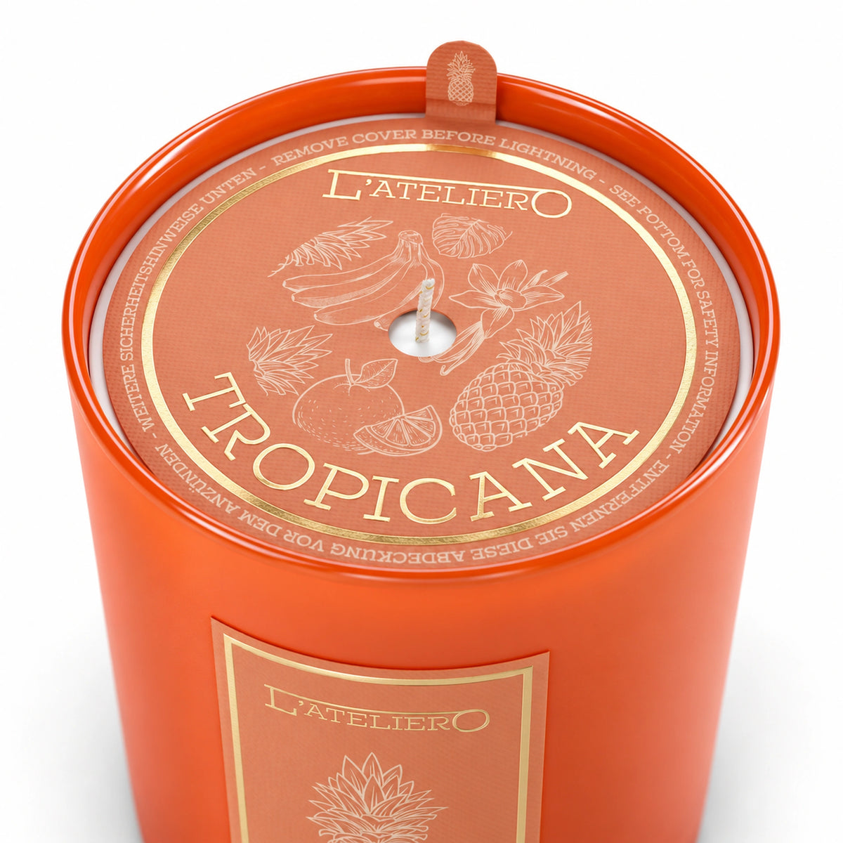 L’ATELIERO Tropicana Duftkerze schräg von oben: oranges Glas und Schutzabdeckung mit goldenen Ananas-, Bananen- und Blütenmotiven.